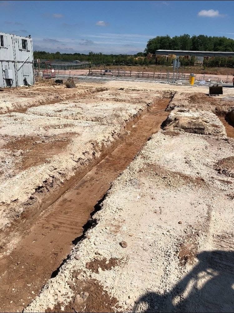 Excavated foundation trenches across a stripped site with a site cabin behind