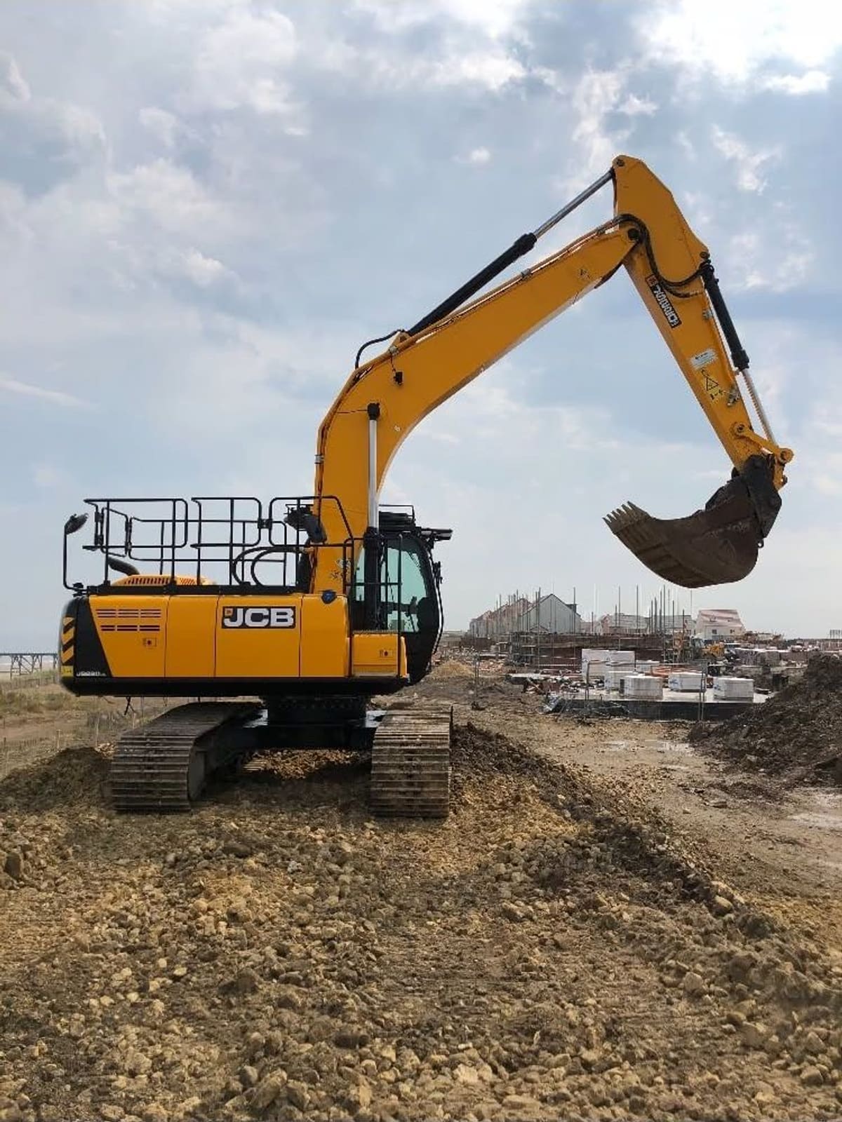 A tracked excavator working on a spoil mound with new houses under construction behind