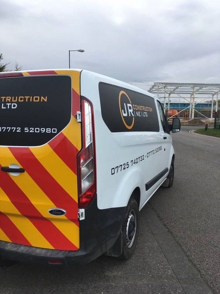 Two liveried J.R Construction vans parked beside a steel-framed building under construction